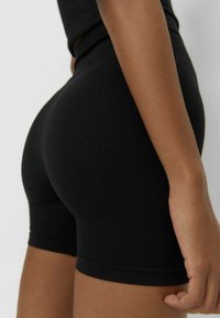 Czarne prążkowane szorty o dopasowanym kroju. Tkanina jest gładka, a szorty sięgają powyżej połowy uda, podkreślając sylwetkę.