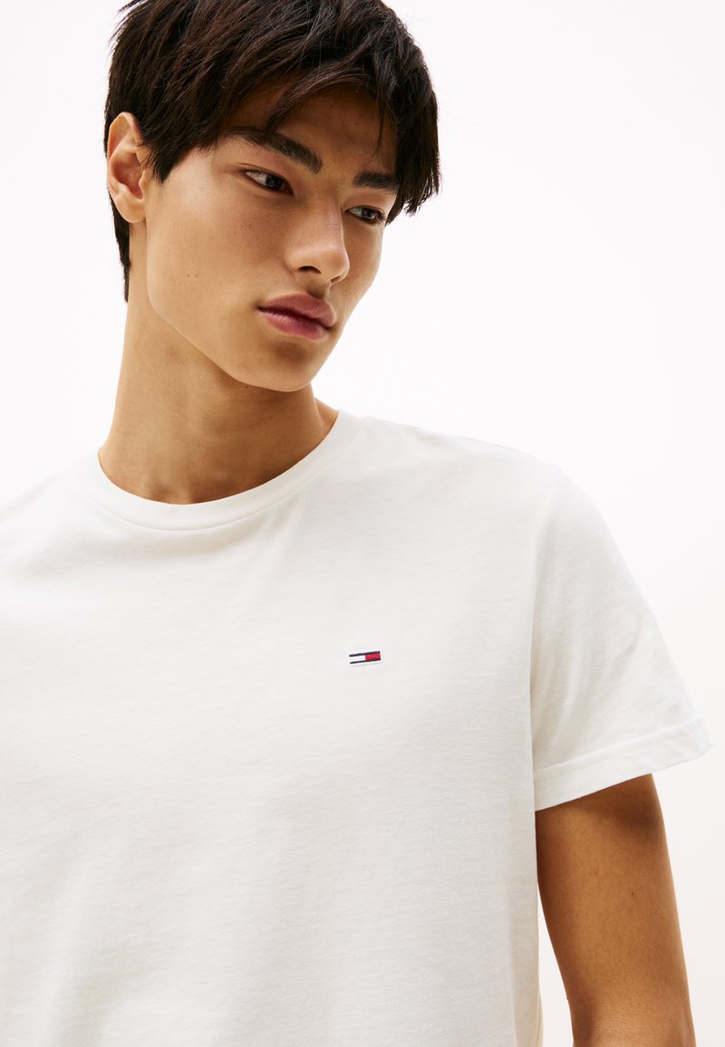 Biała bawełniana koszulka z okrągłym dekoltem, z małym, haftowanym logo na lewej piersi w kolorach czerwonym, białym i niebieskim. Miękka faktura.