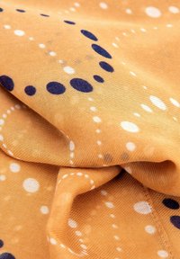 Tessuto di cotone arancione con pois multicolori e motivi circolari in blu scuro e bianco, che mostra una texture liscia e una buona caduta.