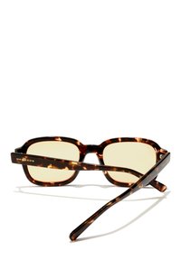 Ochelari de soare cu ramă pătrată groasă din material tartan, lentile cu nuanță galbenă și braț cu emblemă. Material din acetat cu o textură netedă.