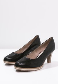 Svarta högklackade skor med texturerad yta, rund tå och träliknande klack. Platt sula med lätt mönstring för grepp.