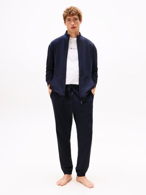 Marineblauwe zip-up jas met hoge kraag, gecombineerd met bijpassende joggingbroek. Beide zijn gemaakt van een gladde stof, met een eenvoudig ontwerp en elastische manchetten.