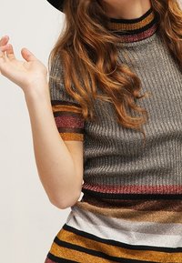 Haut en maille côtelée avec des fils métalliques gris, or et bordeaux en rayures, col montant et manches courtes.