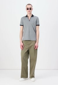 Sivý polo tričko s námorníckym golierom, spárované s voľnými olivovo zelenými nohavicami a bielymi teniskami. Model má na sebe okrúhle slnečné okuliare.