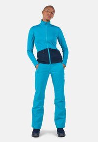 Leichte, türkisfarbene Zip-Jacke mit strukturiertem Oberteil und navyblauem unteren Teil; kombiniert mit passenden türkisfarbenen Hosen; strapazierfähiger Stoff.