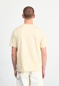 Korte mouwen, ronde hals t-shirt in lichtbeige, gemaakt van zachte stof. Heeft een eenvoudige uitstraling met een rechte zoom en minimale accenten.