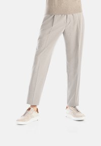 Helle graue, maßgeschneiderte Hose mit Falten, kombiniert mit beigen Sneakers, die Mesh- und Wildlederakzente aufweisen, vor einem weißen Hintergrund.