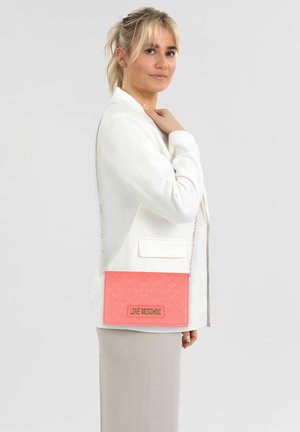 Borsa a tracolla trapuntata corallo con hardware dorato e tracolla a catena. Presenta una forma rettangolare con una placca logo sul davanti. Texture liscia.