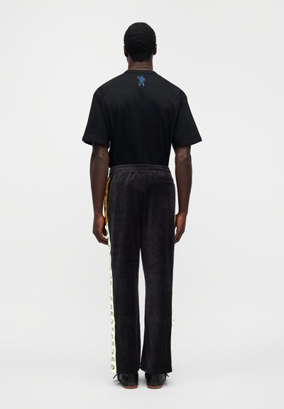 Μαύρο τ-shirt με κοντά μανίκια και μπλε κεντητό σχέδιο. Συνδυάζεται με σκούρο, μαλακό παντελόνι με πλευρικές ρίγες νέον και ελαστική μέση.