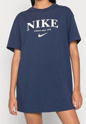 Personne portant une robe t-shirt Nike bleu marine oversize avec un texte blanc « Nike Athletic dept. 1972 » et le logo swoosh sur le devant.