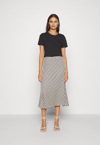 Zwart katoenen t-shirt gecombineerd met een gemusterd midi-rok in crèmekleurige en zwarte tinten, met een uitlopende snit, en witte sandalen met bandjes.