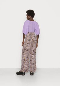 Top lilás com mangas bufantes combinado com calças de cintura alta com estampa floral em roxo, amarelo e preto. Sapatos plataforma pretos completam o visual.