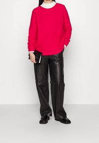 Sweat-shirt fuchsia à manches longues, superposé à un col roulé blanc ; associé à un pantalon large en cuir noir et des chaussures noires.