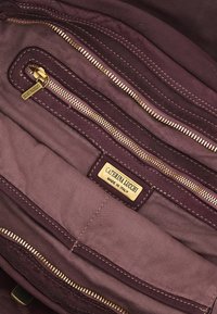 Interno della borsa in pelle di un elegante borgogna scuro, con molteplici tasche con cerniera e un'etichetta del marchio in rilievo dorato. Fodera in tessuto strutturato.