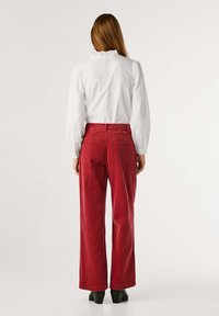 Pantaloni larghi in velluto a coste rossi, tessuto testurizzato, vita alta, tasche posteriori, abbinati a una blusa bianca con colletto arricciato.