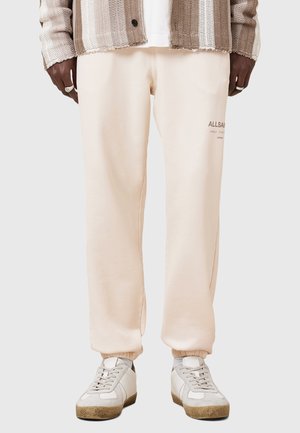 Zachte perzikkleurige sweatpants met een relaxte pasvorm, geribbelde boorden en subtiele "ALLSAINTS" branding. Gecombineerd met lichtgrijze retro sneakers.