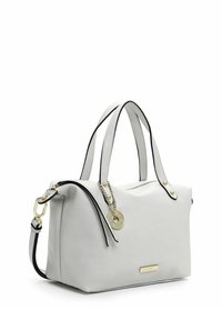 Sac à main en cuir blanc avec garniture noire, doubles poignées supérieures, bandoulière détachable et un charm circulaire doré sur une chaîne attachée à la fermeture éclair.