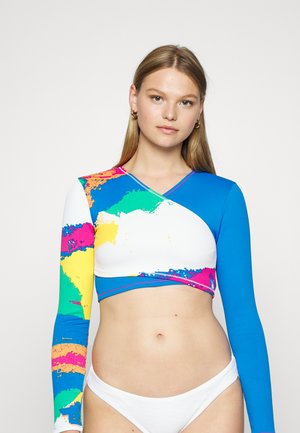 Camisola cropped de manga longa colorida, apresentando uma mistura de padrões vibrantes em azul, branco e com aspeto de tinta. Textura canelada com decote em V.