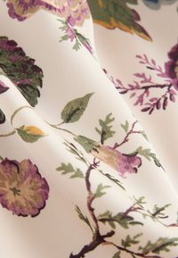 Weißer Stoff mit einem floralen Muster mit violetten, grünen und gelben Blumen und Blättern, dargestellt mit weichen Falten und Textur.