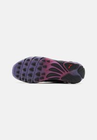 Suela de zapato con parte superior negra flexible, acentos en púrpura y rojo, suela de goma texturizada con patrones de tracción circulares.
