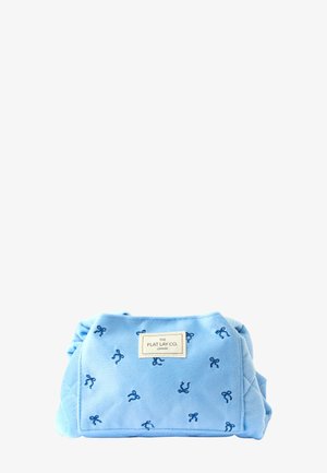 Borsa morbida in peluche azzurro con motivi a fiocco blu scuro e un'etichetta sul davanti. Design compatto con bordi arrotondati e lati arricciati.