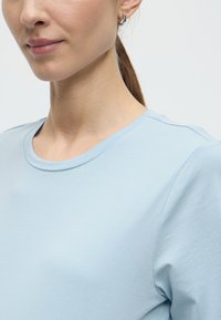 Ανοιχτό μπλε κοντομάνικο πουκάμισο από απαλό, λεία ύφασμα με στρογγυλή λαιμόκοψη. Διακριτικός ραφές χωρίς ραφές στους ώμους και λεπτή υφή.