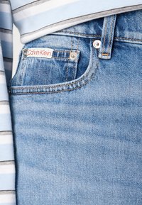 Lichtblauwe denim jeans met een subtiele textuur, voorzien van een rood-witte Calvin Klein-label op de voorkant van de broekzak en een drukknoopsluiting.