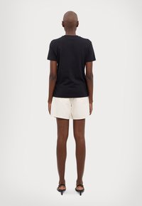 Czarna bawełniana koszulka z okrągłym dekoltem, zestawiona z beżowymi szortami. Szorty mają postrzępione wykończenie i tylne kieszenie; oba elementy mają luźny krój.