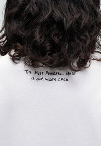 Abbigliamento in cotone bianco con una citazione scritta a mano in nero sul retro che recita: "LA MUSA PIÙ POTENTE È IL NOSTRO BAMBINO INTERIORE."