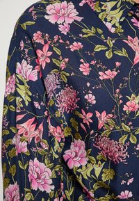Blusa di seta blu navy con motivo floreale caratterizzata da fiori rosa e verdi, dettagli intricati e una consistenza liscia.