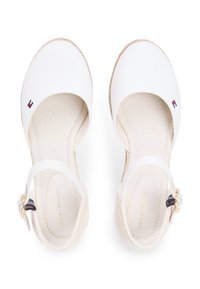 Espadrilles en toile blanche avec bout ouvert, bride autour de la cheville et semelle en jute tressé. Inclut un petit détail de logo en rouge, blanc et bleu.