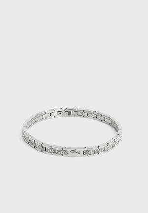 Bracelet chaîne en argent avec des maillons rectangulaires, certains sertis de petits cristaux et un fermoir avec un logo crocodile embossé.