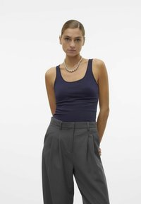 Top aderente blu navy realizzato in tessuto elasticizzato, abbinato a pantaloni gray a vita alta con pieghe. Presenta un collo rotondo e spalline sottili.