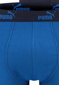 Blaue Baumwoll-Boxershorts mit einem schwarzen Elastikbund, der mit blauen "PUMA"-Schriftzug und einem kleinen Logo versehen ist. Glatte Textur; klassischer Schnitt.