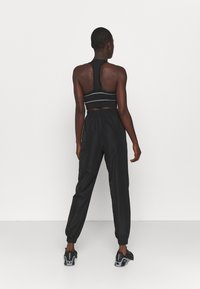 Černá sportovní podprsenka s designem racerback a šedými horizontálními pruhy, doplněná černými tepláky s elastickým pasem a zúženými lemy.