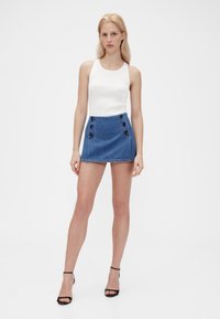 Fehér bordázott trikó magasderekú farmer miniszoknyával, mely sötét gombdíszítéssel és rojtos szegéllyel rendelkezik. A fekete magassarkú cipő egészíti ki a megjelenést.