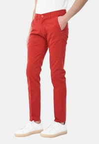 Chinos rossi in cotone con una vestibilità slim, dotati di tasche anteriori e chiusura a bottone, abbinati a sneaker bianche e una camicia neutra.