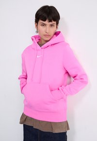 Roze hoodie gemaakt van zachte stof met een voorzak. Voorzien van trekkoorden en een klein wit logo op de borst.