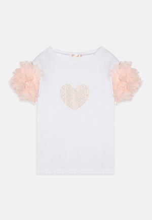 Maglietta bianca di cotone con maniche corte a sbuffo realizzate in tulle rosa chiaro morbido e leggero. Presenta un disegno di un cuore perforato al centro.