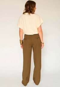 Haut beige à manches courtes associé à un pantalon large taille haute marron avec deux poches au dos et une texture subtile.