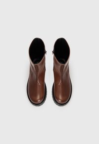 Par črnih usnjenih gležnjarjev rjave barve z črnimi podplati in stranskimi zadrgami, prikazanih pokončno na belem ozadju.