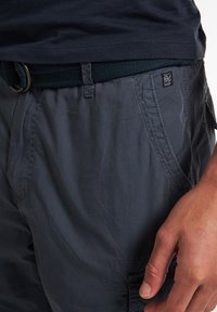 Mørkegrå, letvægts cargo shorts med flere lommer, subtil glans og syet detaljering, parret med et vævet sort bælte.
