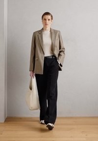 Hellbraunes, gestreiftes Blazer über einem gerippten weißen Top, kombiniert mit schwarzen Hosen und einer cremefarbenen Handtasche. Die Schuhe sind hellbeige und flach im Design.