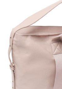 Sac à épaule en cuir rose clair avec une texture lisse, présentant une large sangle et un accent matériel subtil sur le côté.