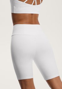 Shorts albi, cu talie înaltă, dintr-un material neted, cu un design ajustat care se extinde până la mijlocul coapsei, având un branding minim pe talie.