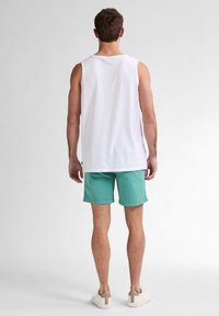 Débardeur blanc sans manches, shorts turquoise et baskets claires. Le débardeur a une coupe décontractée, tandis que les shorts ont une coupe droite.