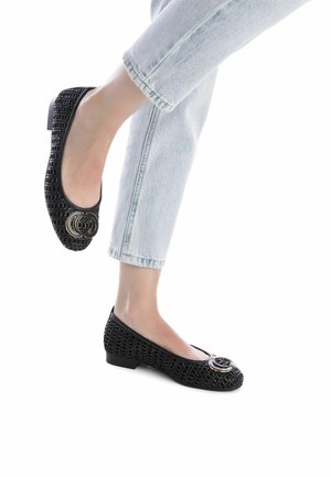 Bailarinas negras con un diseño tejido texturizado, punta redondeada y un acento de logo metálico. Tacón bajo en bloque. Combinadas con unos vaqueros claros con dobladillo.