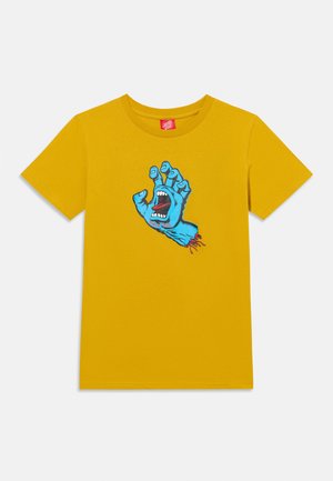 Mosterdgele T-shirt met korte mouwen met een afbeelding van een blauwe hand met een open mond en tong op de palm, vingers omhoog gekruld.