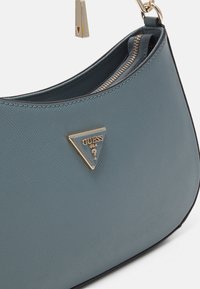 Ljust blå strukturerad handväska med en guldtonad triangulär logotypaccent och ett dragkedjsöppning. Tillverkad av slitstarkt material med en slät yta.