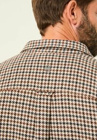 Hahnentritt-Muster Hemd in Beige, Braun und Schwarz. Mit Kragen, gestickten Details und einem dezenten Logo auf der Rückseite. Textil mit Struktur.